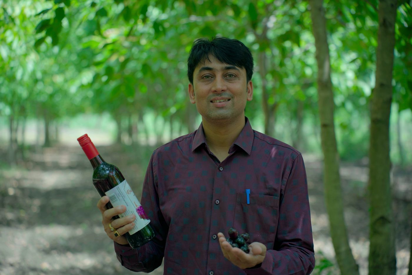 Devendra Singh Patel standing among the jamun trees, holding a bottle and a handful of freshly picked fruit.