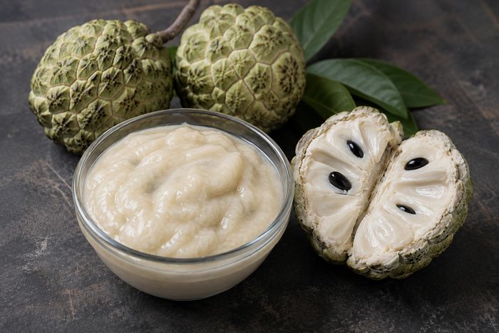 Pale custard apple pulp in a bowl with a whole sitaphal alongside.