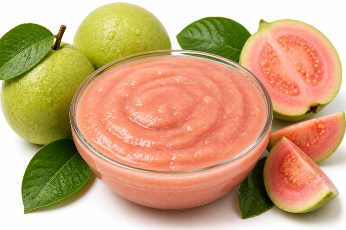 Guava cut open to show the pink flesh, beside whole fruit.